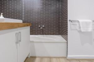a bathroom with a white tub and a black tile wall at Bay View Style in Lorne +12 photos