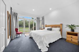 a white bedroom with a bed and a red chair at Renall St Gem Central Masterton in Masterton +22 photos