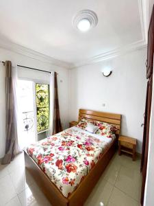 a bedroom with a bed with a floral comforter and a window at sidof Redence L&A in Yaoundé