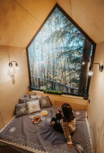 a woman sitting on a bed in a room with a large window at Domek na drzewie Ceprowo in Szczyrk