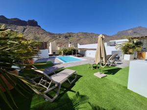 a patio with lawn chairs and an umbrella and a pool at Casa Federico & Manuela – Piscina Climatizada in Mogán
