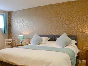 a bedroom with a bed with white sheets and gold wallpaper at Park View Cottage in Stranraer