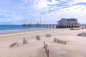 a beach with a pier and a house and the ocean at Paradise Found - Nags Head MP 16.5, Oceanfront, Ocean & Sound Views, Pool, Hot Tub, Pets OK in Nags Head