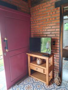 a living room with a tv and a brick wall at Chalé lindo e confortável! in Massaranduba