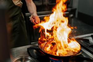 a person cooking food in a pan with flames at Hotel LIDO in Jurata