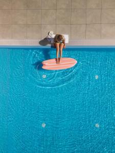a woman sitting on a surfboard in a swimming pool at Hotel LIDO in Jurata