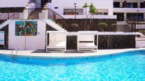 a swimming pool with two white chairs next to a building at Coral Los Alisios in Los Cristianos