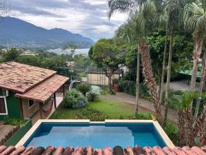 a swimming pool next to a house with palm trees at Micas House in Ilhabela