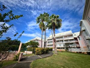 a building with palm trees in front of it at Horizon Doré Appt avec piscine - vue sur mer in Gourbeyre