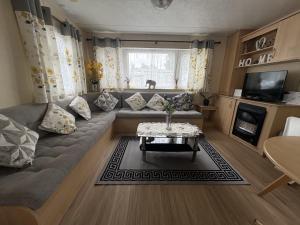 a living room with a couch and a table at Bright Family Caravan with Deck & BBQ at Seawick Holiday Park, Clacton in Clacton-on-Sea