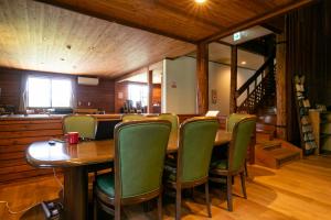 a dining room with a wooden table and green chairs at みみずく山荘 Mimizuku Lodge in Myoko