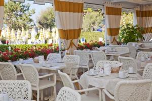 un comedor con mesas blancas, sillas y flores en Hotel Alexander, en Caorle