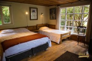 two beds in a room with two windows at Posada Queulat in Puerto Puyuhuapi