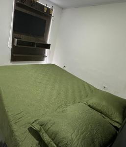 a bed with a green comforter in a room at KITNET mobiliada com ar condicionado in Guarujá