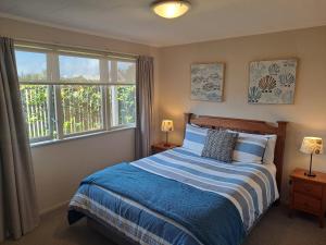 a bedroom with a bed with blue and white sheets and windows at Feel at Home in Tauranga