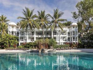 a large white building with palm trees in front of a pool at Peppers Beach Club & Spa in Palm Cove