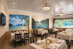 a restaurant with white tables and chairs and a large painting at Thành Trung Motel in Cat Ba
