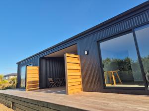 a black house with large windows and a wooden deck at Accomodation at Curio in Curio Bay