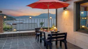 a table with chairs and a red umbrella on a balcony at That Day's Namhae Ocean View Pension in Namhae
