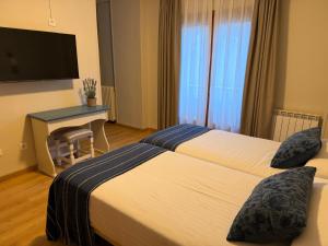 two beds in a hotel room with a desk and a television at Edelweiss Hotel in Torla-Ordesa +70 photos