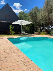 a swimming pool with an umbrella and a table and chair at Soeterus Guest Farm in Calitzdorp