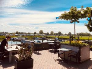 a woman sitting at a table at a restaurant overlooking a marina at Bell Tent aan de haven in Heerewaarden