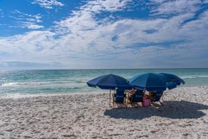 two chairs and two blue umbrellas on a beach at Chic first-floor condo with Gulf & pool view & pickleball - steps to beach in Santa Rosa Beach