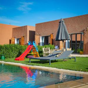 a playground with slides and an umbrella next to a pool at Dar Fatma Charming Moroccan Guesthouse with Pool & Hammam in Sidi Bibi
