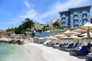 a beach with chairs and umbrellas in front of a hotel at Buzë Boutique Hotel in Sarandë