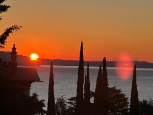 a sunset over the water with cypress trees in the foreground at Seeblick VILLA LAGUNA BLUE - Private Spa - Whirlpool & Sauna in Gardone Riviera +35 photos