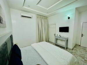 a white bedroom with a bed and a television at The Cape - Apartment in Bamgbose