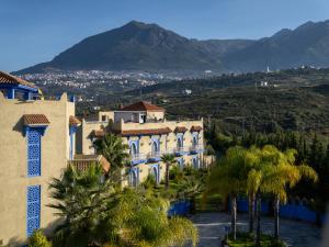 a building with palm trees in front of a mountain at Dar Ba Sidi & Spa Chefchaouen in Chefchaouen