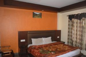 a bedroom with a bed with an orange wall at Hotel Tridev Manali in Manāli