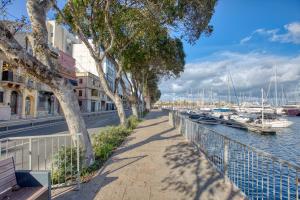 a sidewalk next to a river with boats at Valletta Marina View - Seafront Apartment in Tal-Pietà