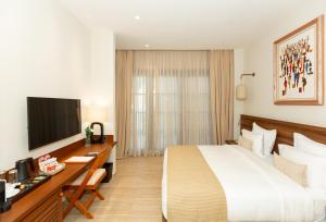 a hotel room with a bed and a desk with a television at Native Hotels Ouidah in Kika
