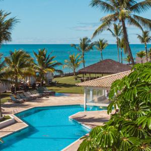 a resort swimming pool with palm trees and the ocean at Saint Tropez Praia Hotel in Arraial d'Ajuda +20 photos