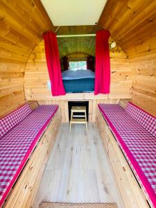 a room with two beds in a wooden cabin with red curtains at Barrel Cabin 2 in Trethurgy
