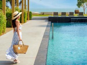 a woman in a hat walking by a pool at SO/ Sofitel Hua Hin in Cha Am