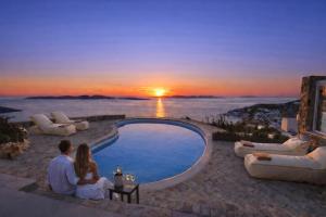 a man and woman sitting around a pool watching the sunset at Villa Tavani Agios Ioannis Mykonos in Agios Ioannis Mykonos