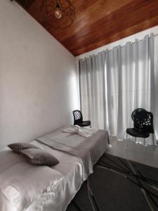 a bedroom with a bed with two chairs and a window at Loftshorizontedesalvina in Búzios