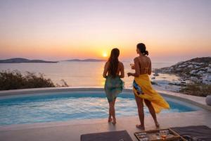 two women standing next to a swimming pool watching the sunset at Villa Vanita Agios Ioannis Mykonos in Agios Ioannis Mykonos