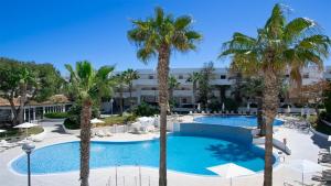 a pool with palm trees in front of a building at BLUESEA Es Bolero in Cala d´Or