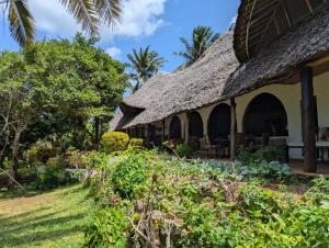 a house with a thatched roof and a garden at Sansuri Dreams Beach House in Msambweni
