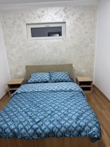 a bedroom with a bed with a blue comforter and two tables at Timi&Amos2 in Caransebeş