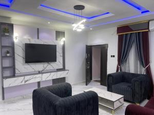 a living room with a flat screen tv and two chairs at Knock inn luxury apartment in Benin City