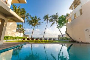 a swimming pool in front of a building with palm trees at Kixi Beach in Unawatuna