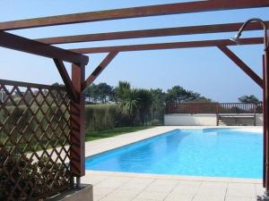 a swimming pool with a wooden pergola next to at Maisonnette 6 pers- Piscine commune - Plage à 500 m- LOEIZ in Guidel-Plage