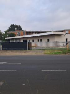 a white building with a fence next to a street at THEMBAGUESTHOUSe in Benoni
