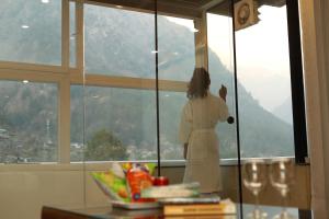 a woman standing in front of a window looking out at The Udit By West Western - Central Heated and Air Cooled - River View & Roof Top cafe & Bar in Kasol