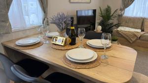 a wooden table with plates and wine glasses on it at Big Boss Caravan-Camber Sands,Sleep 8, Free Wi-Fi, Netflix, Parking in Camber